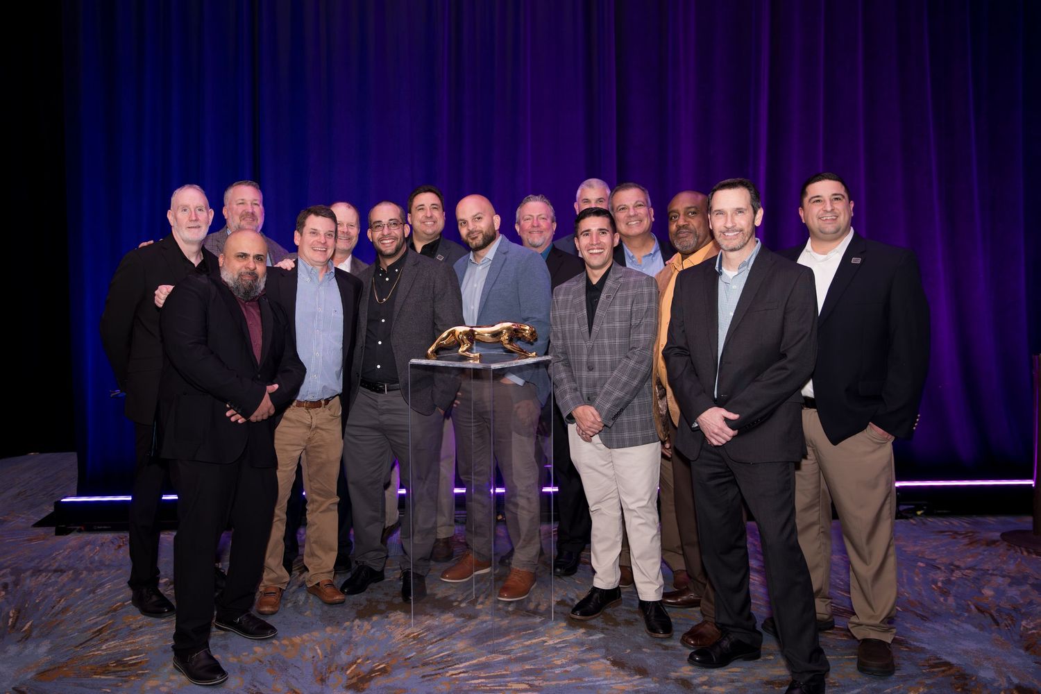 Group of professionals posing together at a formal awards ceremony on a staged event venue with purple lighting.