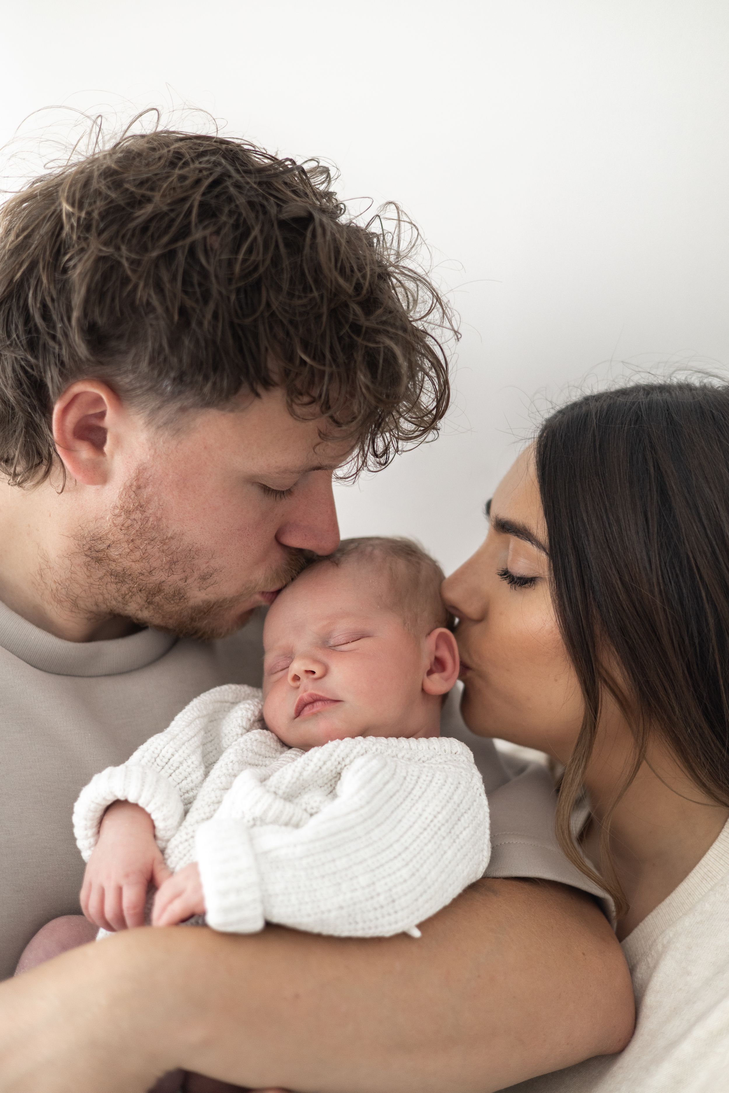 Father gently holding and kissing his newborn baby during a natural family photograph