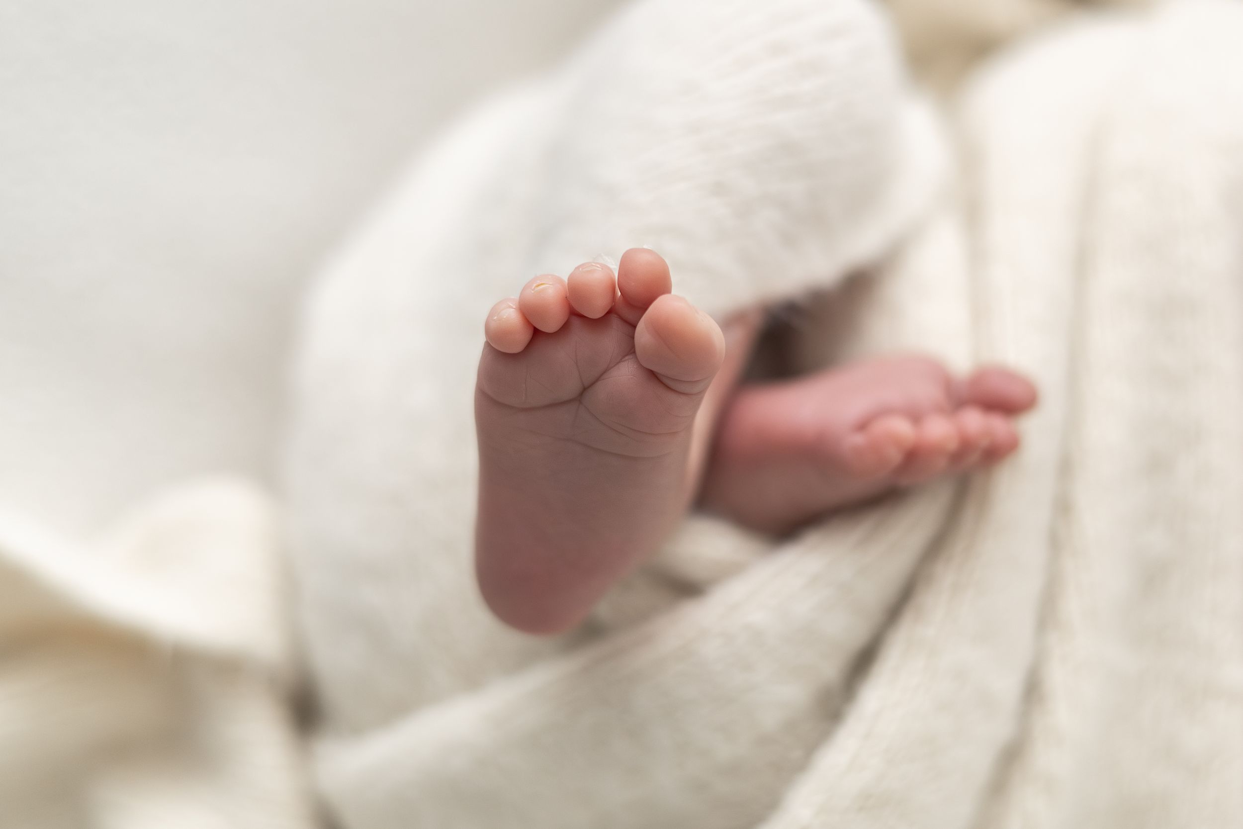 Close-up photograph of a newborn baby's tiny feet resting against a soft neutral blanket