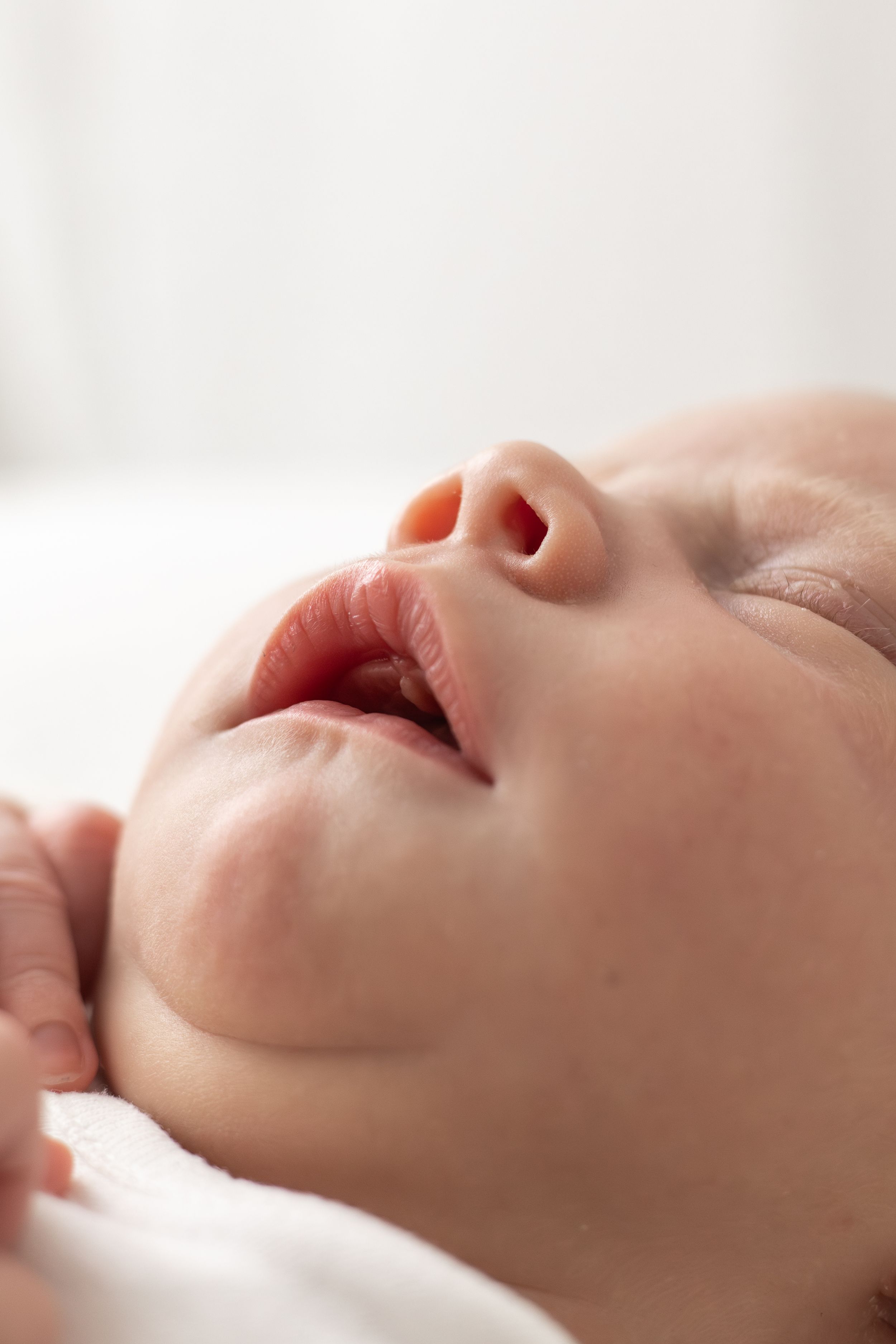 Close-up of a peaceful newborn baby's face with slightly parted lips, lying on a white surface.