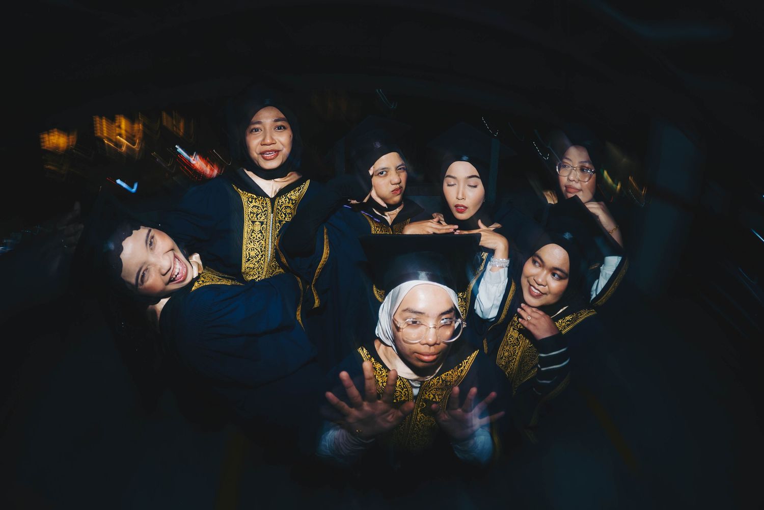 Group of young women in graduation attire holding glowing phones in a dark setting.