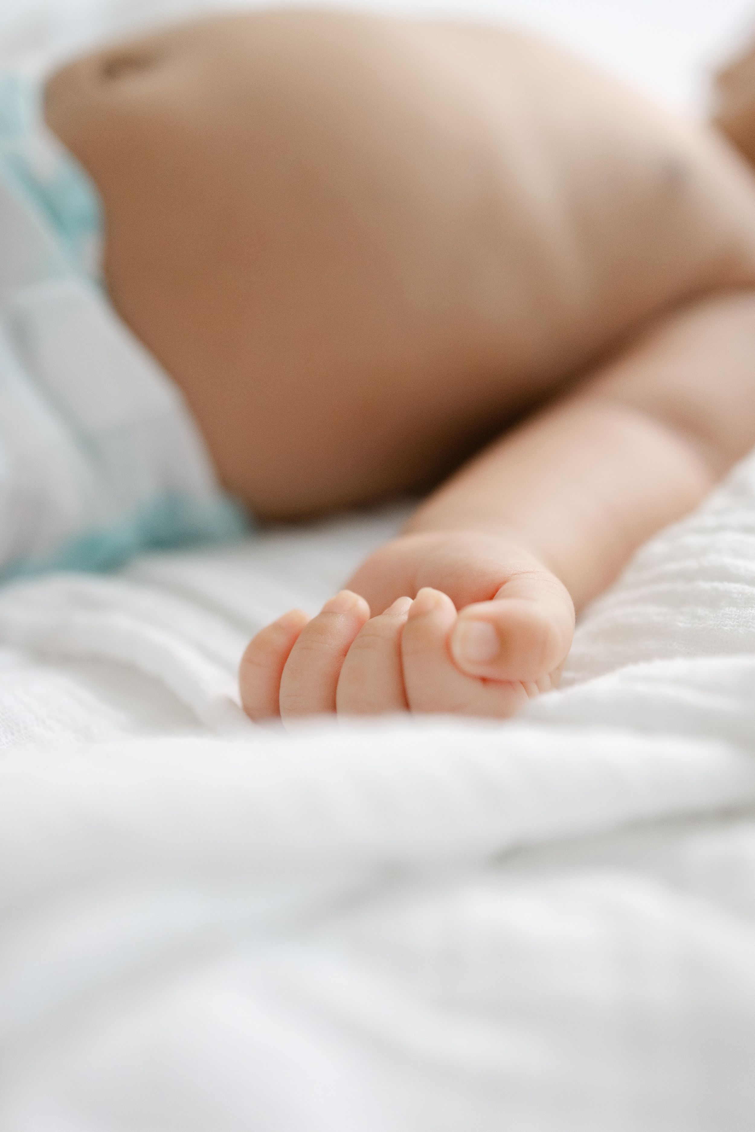 Close-up of a newborn baby hand resting on a soft white blanket while lying in a diaper.