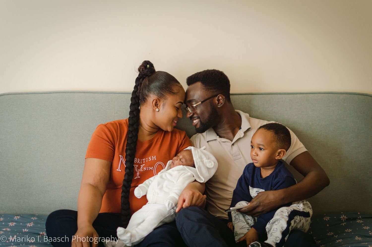 A loving family of four shares an intimate moment on a couch, parents gazing at each other with their two children.