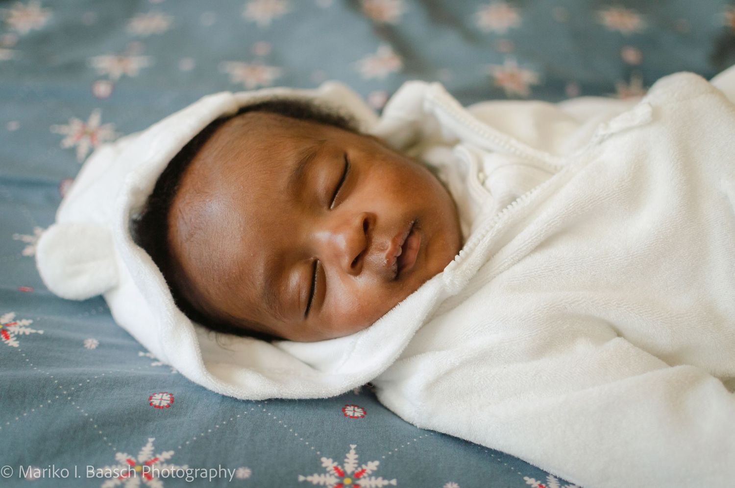 A peaceful newborn baby sleeps soundly wrapped in a white swaddle with a soft hood during a lifestyle session.