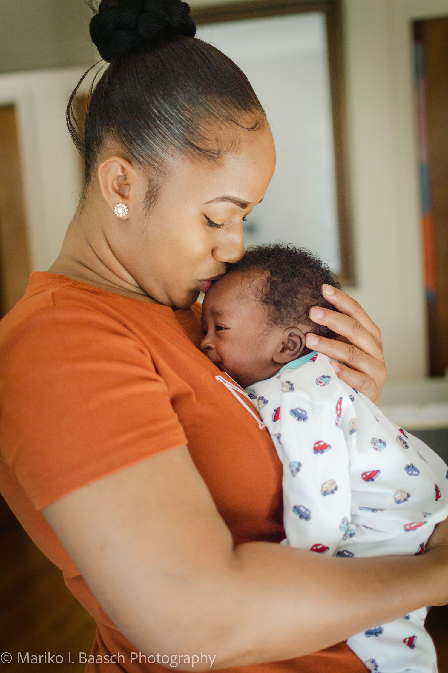 A mother tenderly kisses her newborn babys forehead while cradling them close in a heartfelt portrait.