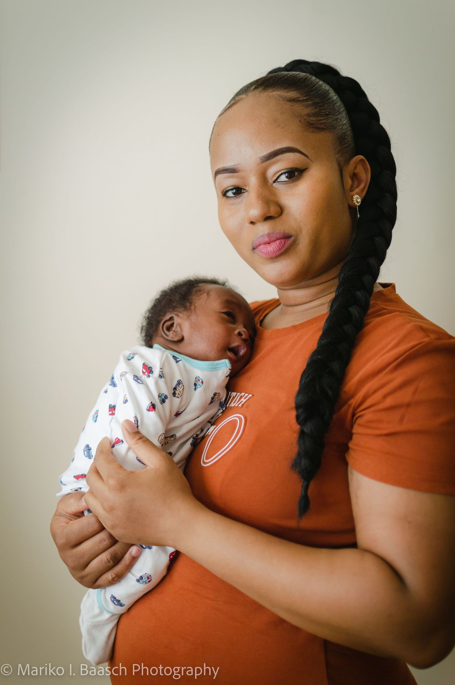 A mother in an orange shirt holds her newborn baby against her chest in a classic lifestyle newborn portrait.