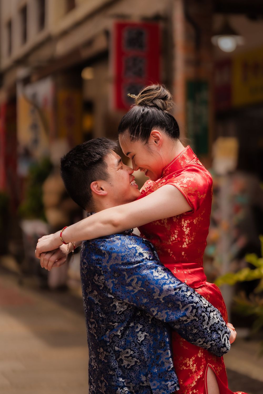 Couple in traditional Chinese qipao embracing romantically on a street in Chinatown.