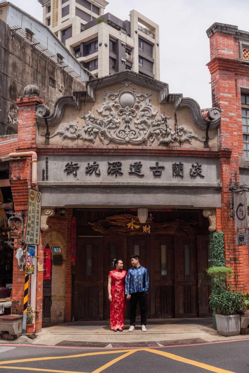 Couple in traditional Chinese attire posing at ornate Tamsui Old Street entrance with red brick architecture in Taiwan.