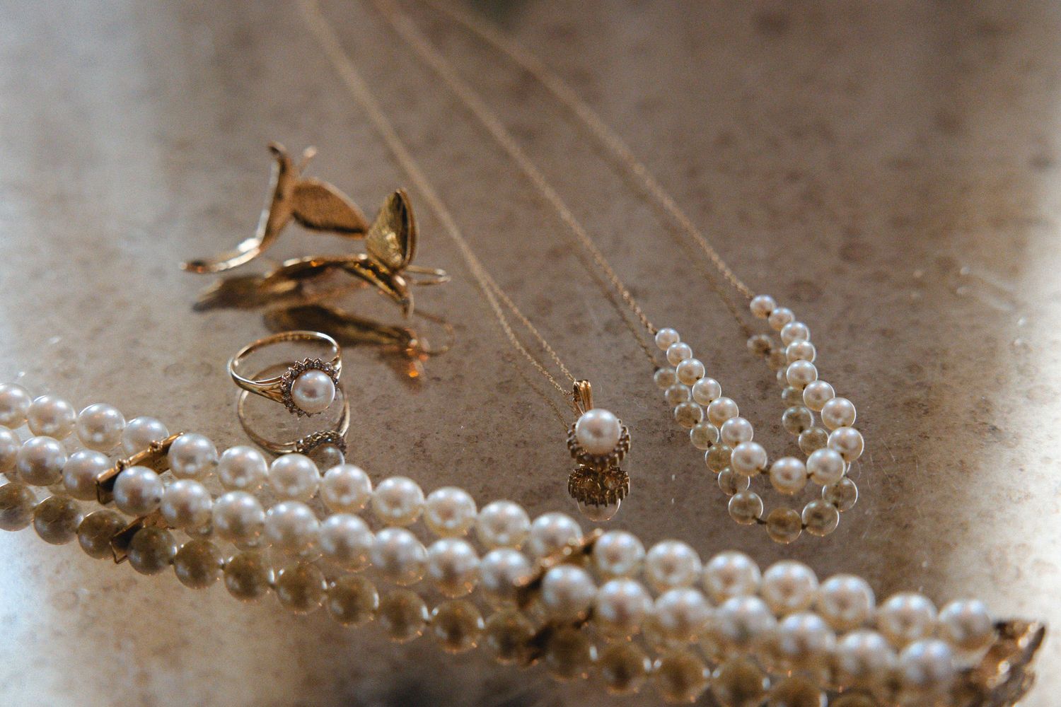 Gold and pearl jewelry collection including necklaces and brooches arranged on a marble surface.