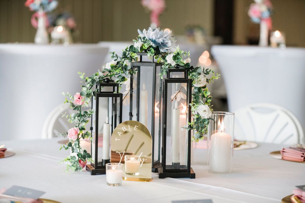 Elegant wedding centerpiece with black lanterns, white candles, and pink and white floral arrangements on a white tablecloth.