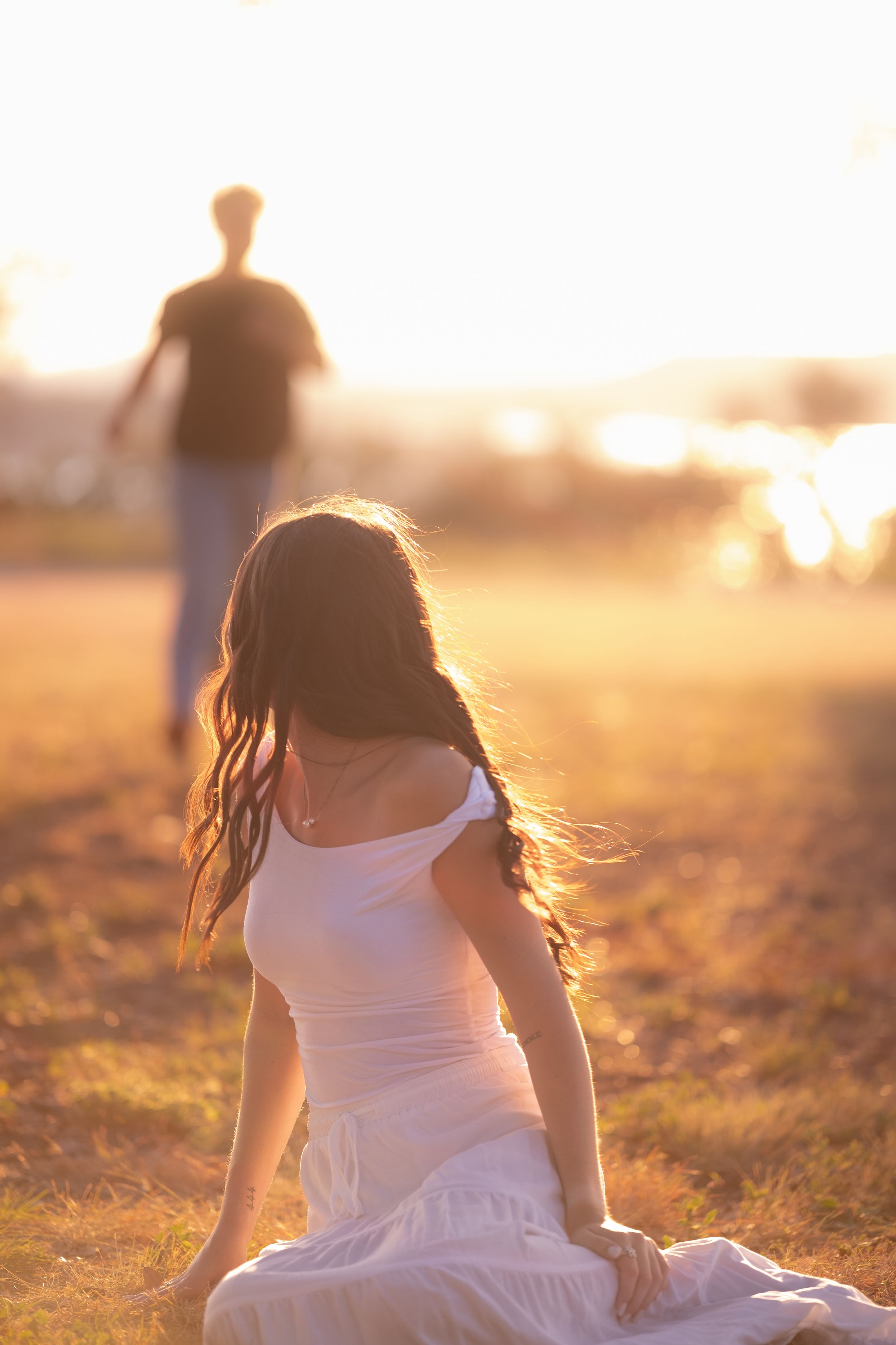 Woman in white dress sitting in a golden field as a man approaches in Belton Texas