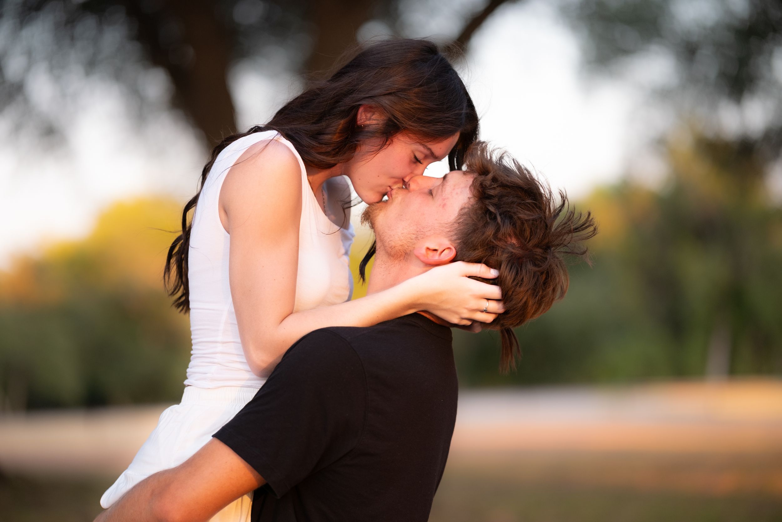 Couple sharing a passionate kiss outdoors with warm golden light behind them in Belton Texas