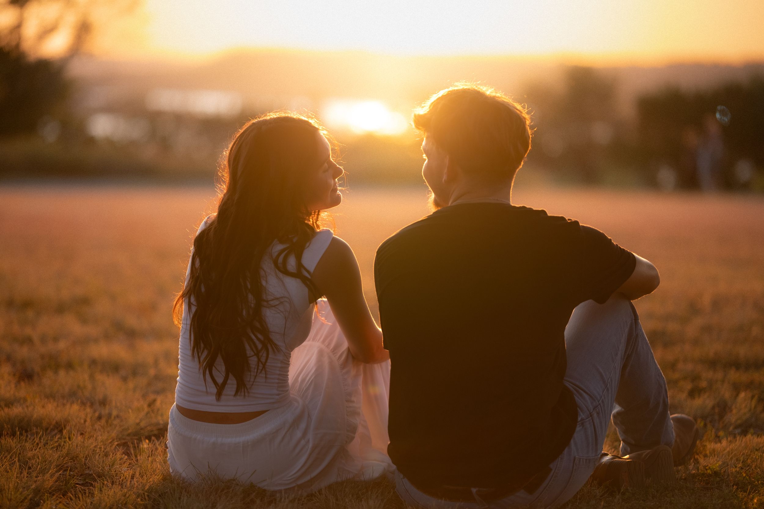 Couple sitting in a golden field at sunset, holding hands and gazing at each other romantically in Belton Texas