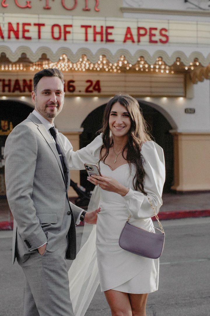 Couple in wedding attire posing outside a movie theater with Planet of the Apes marquee lights.