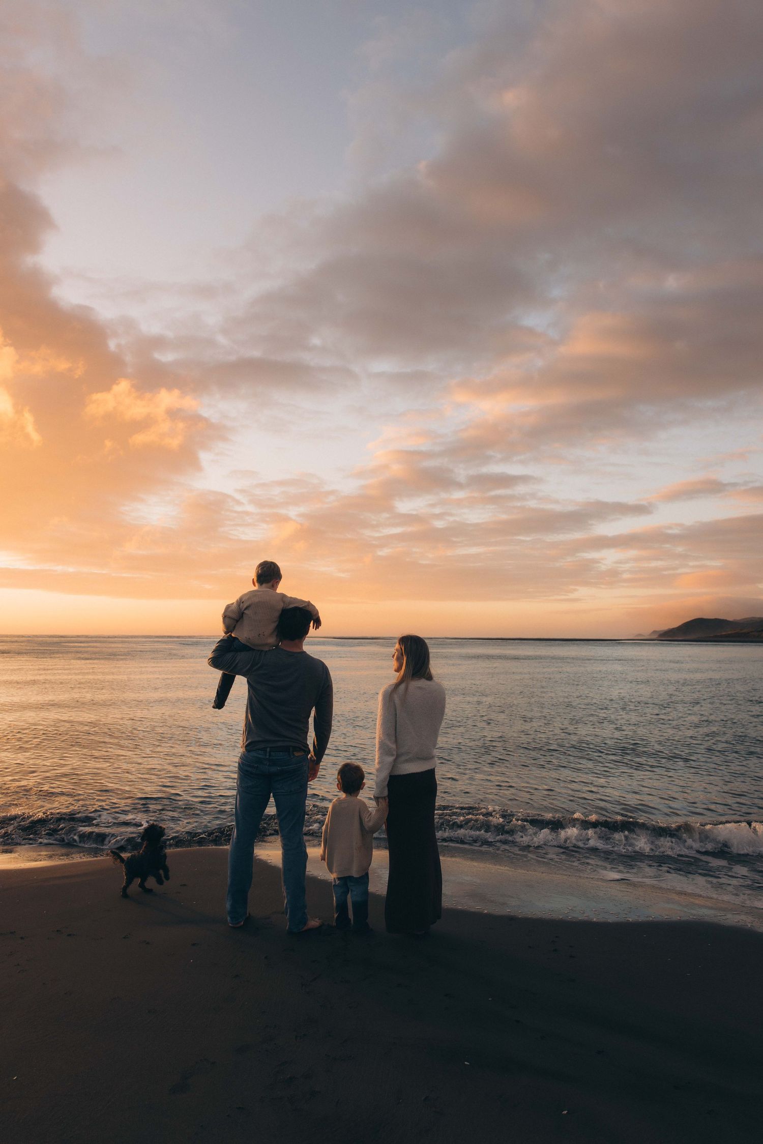 Family of four with a dog standing on a beach at sunset, Raglan Waikato New Zealand.