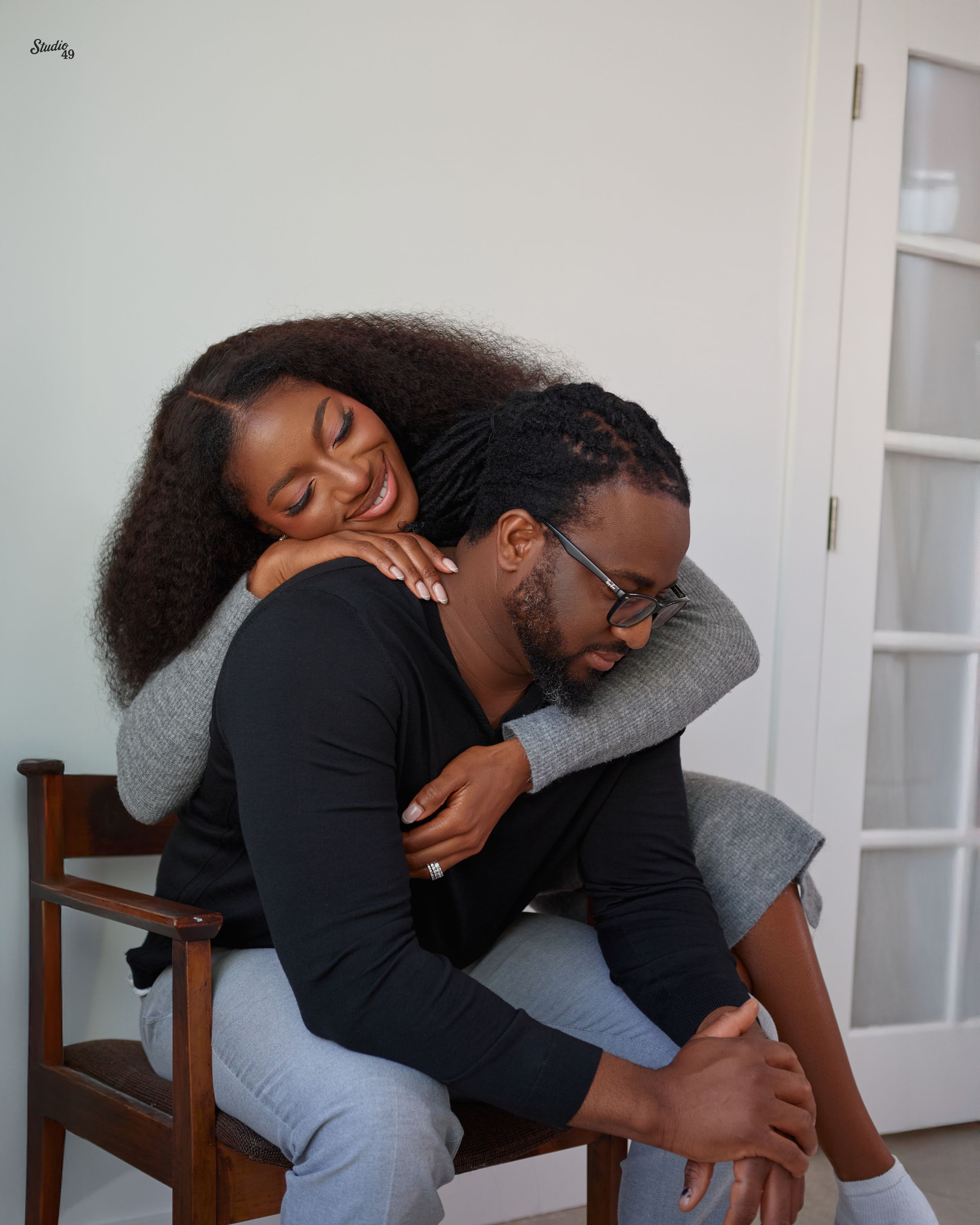 Affectionate couple embracing in cozy indoor setting, woman hugging man from behind.