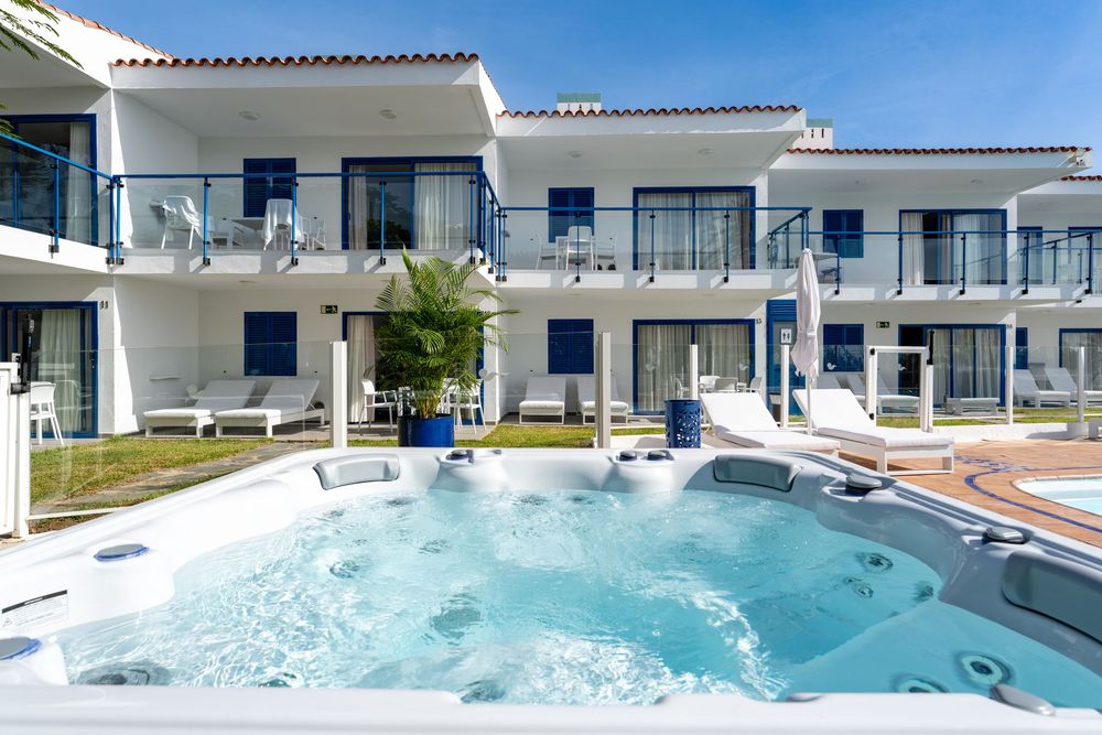 Luxurious outdoor hot tub jacuzzi in front of a white and blue Mediterranean villa with balconies and sun loungers.
