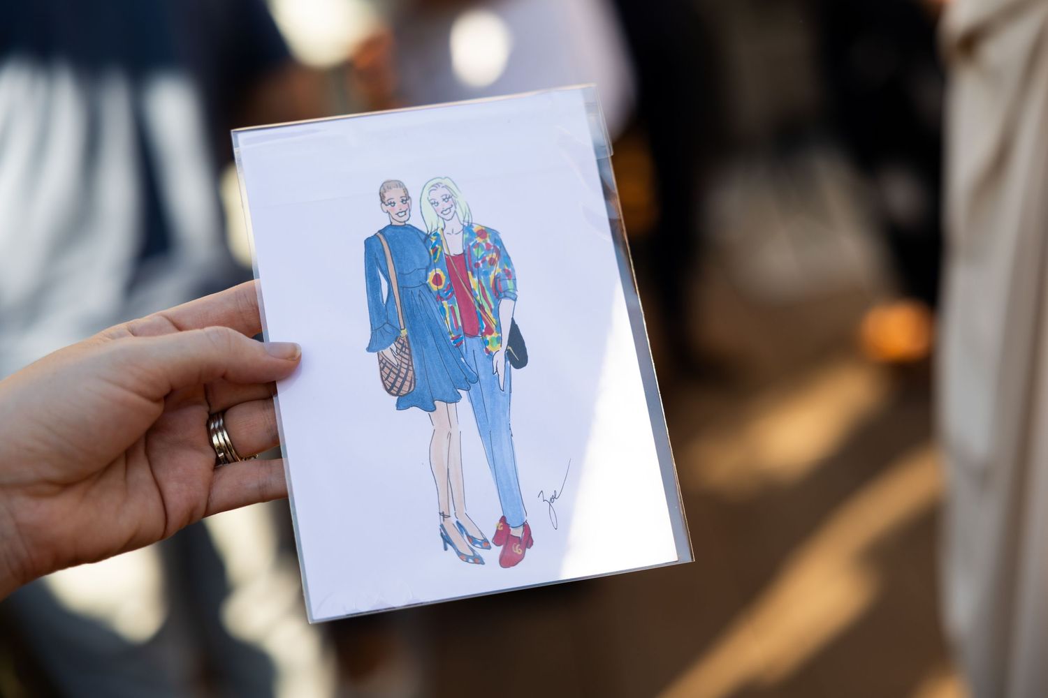 Person outside holding illustration of two women chatting with drinks.