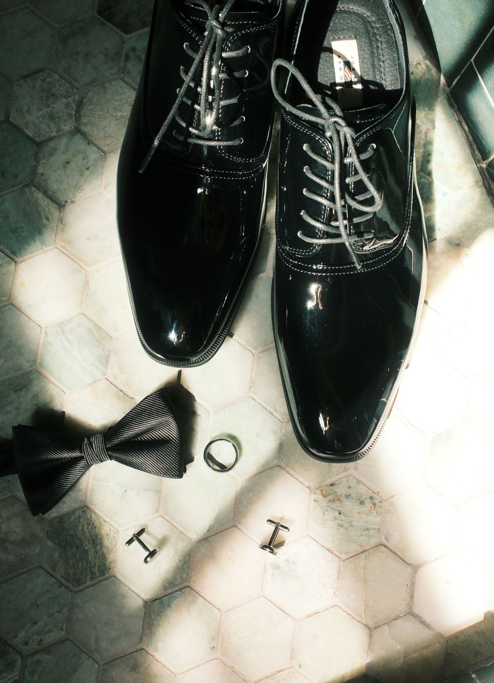 Grooms wedding accessories flat lay featuring black patent leather oxford shoes bow tie and cufflinks.