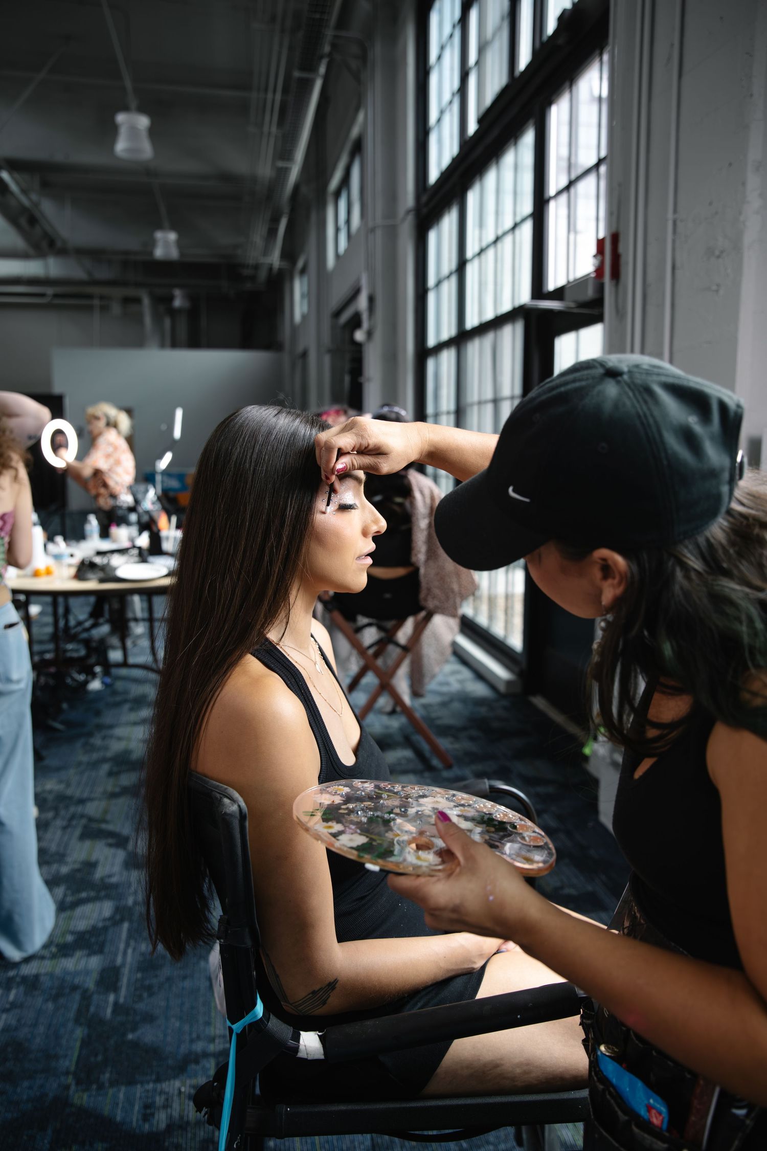 Makeup artist applying cosmetics to a model backstage at a fashion show in a studio setting.