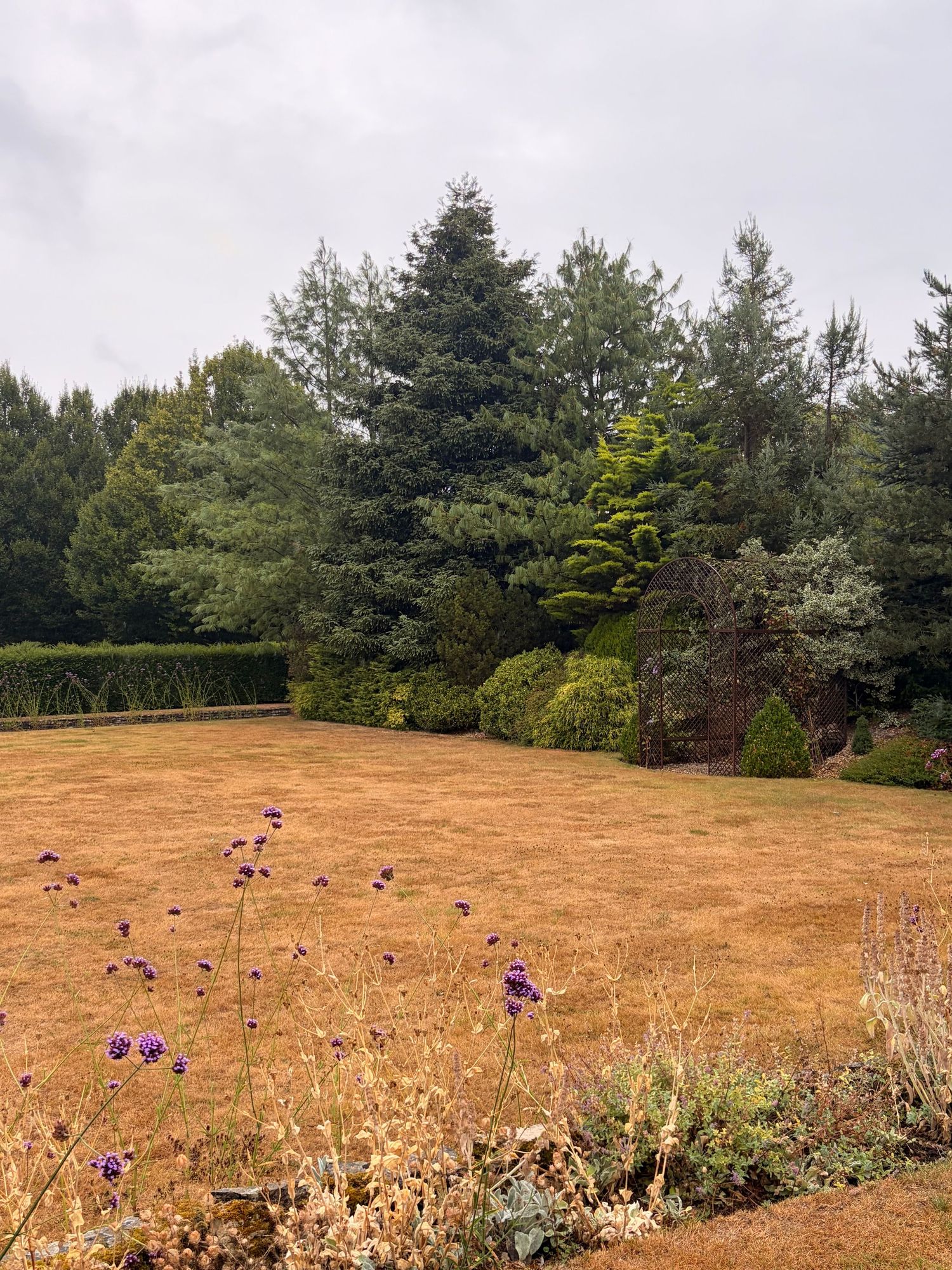 A charming oast house with a conical roof, surrounded by lush gardens and brick steps in the English countryside.