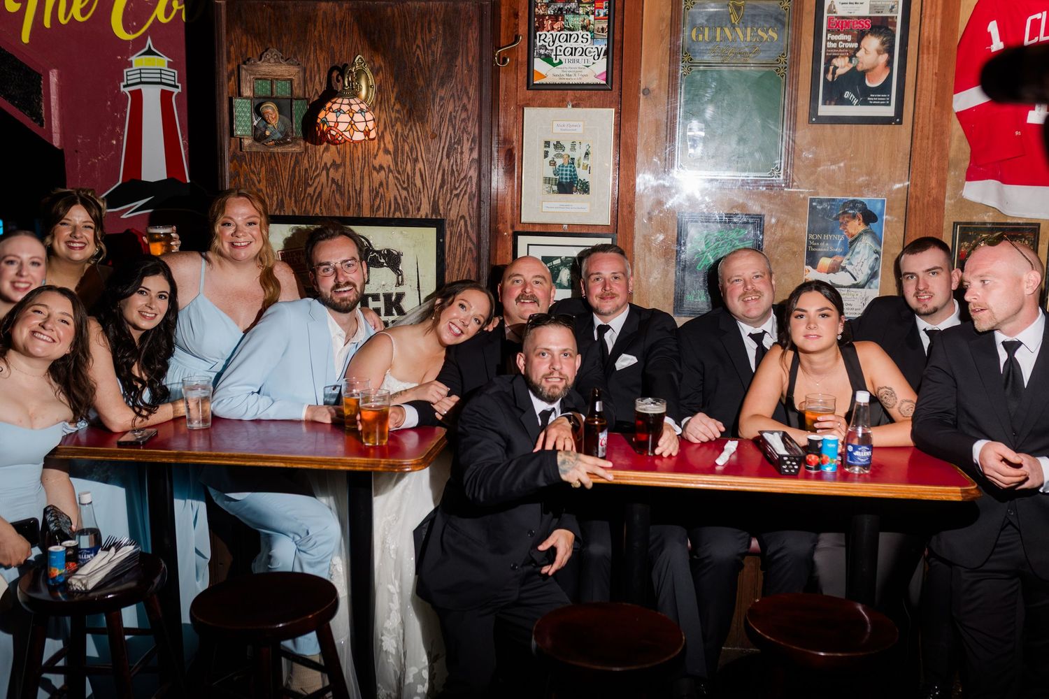 Large wedding party group photo smiling together in a cozy bar decorated with vintage posters and memorabilia.