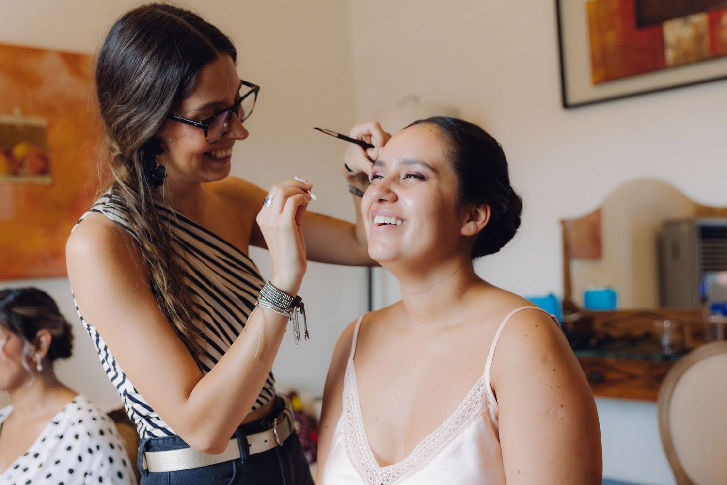 Makeup artist applying eyeshadow to smiling bride during wedding preparation.