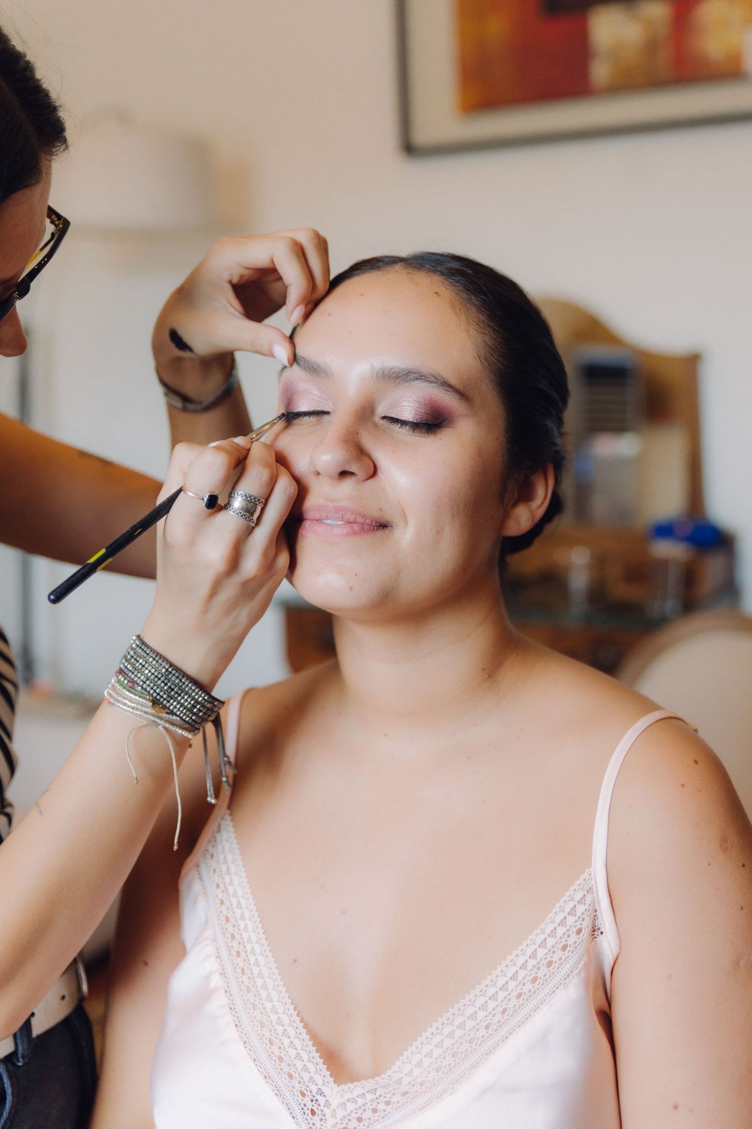 Professional makeup artist applying eye makeup to bride in white slip dress.
