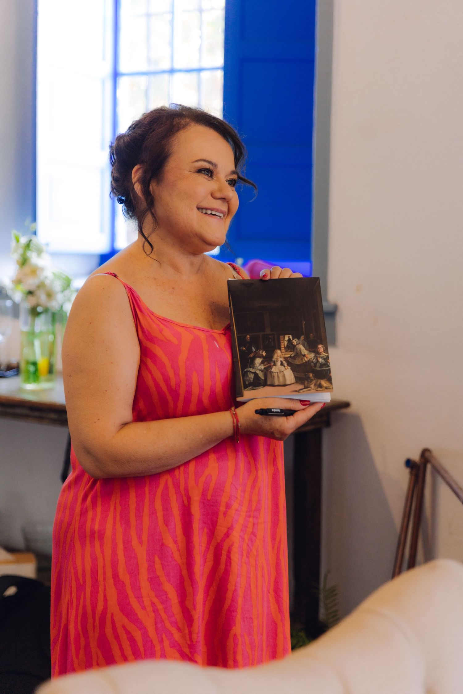 Woman in pink zebra print dress holding art book at wedding venue.