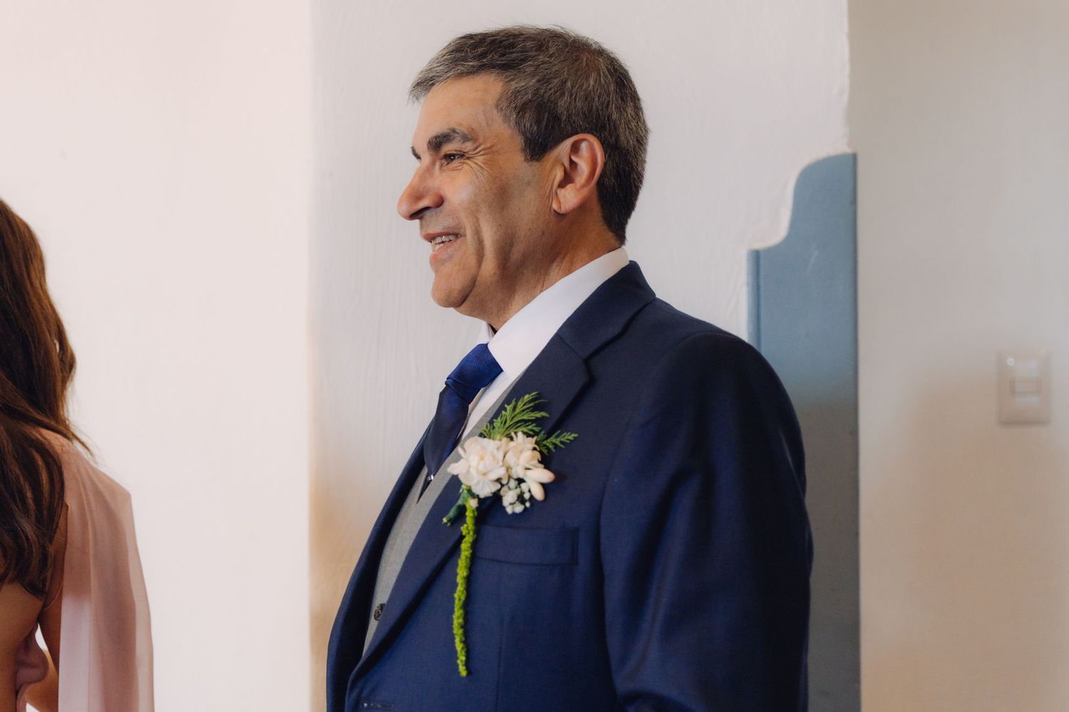 Smiling man in navy blue suit with floral boutonniere at a wedding ceremony.