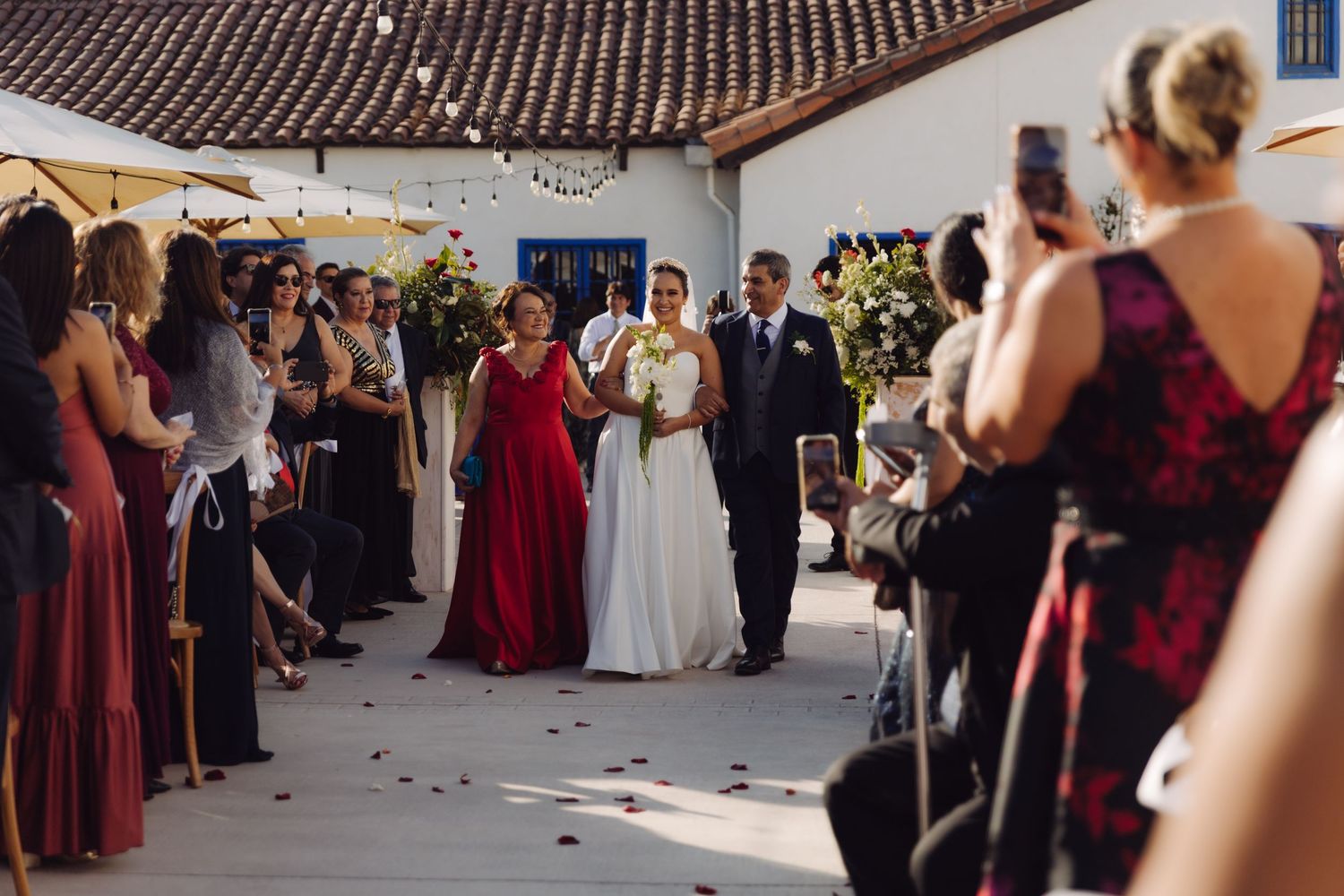 Bride in white gown walks down outdoor aisle with escort at wedding ceremony.