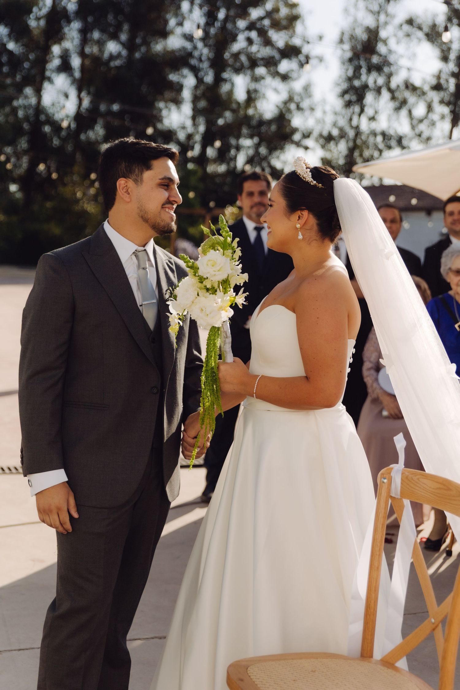 Bride and groom share a tender moment at outdoor wedding ceremony, bride holding white floral bouquet.