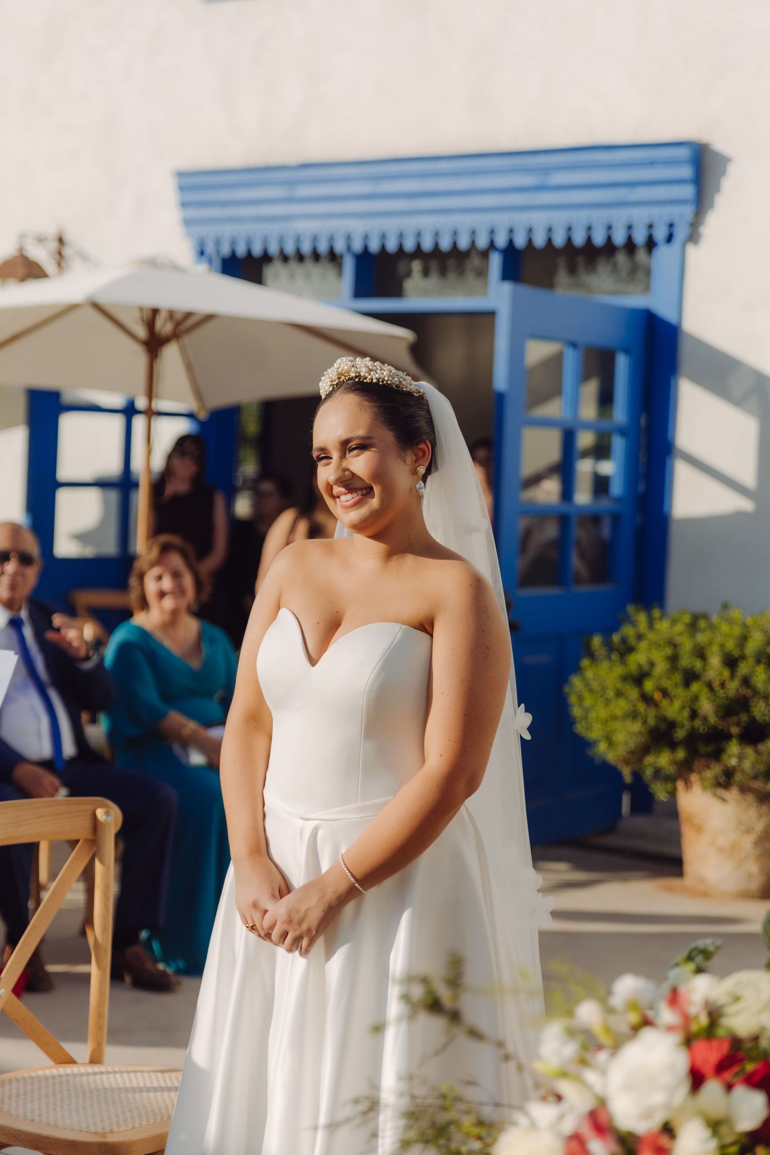 Beautiful bride in white strapless gown and tiara smiles at outdoor wedding ceremony.