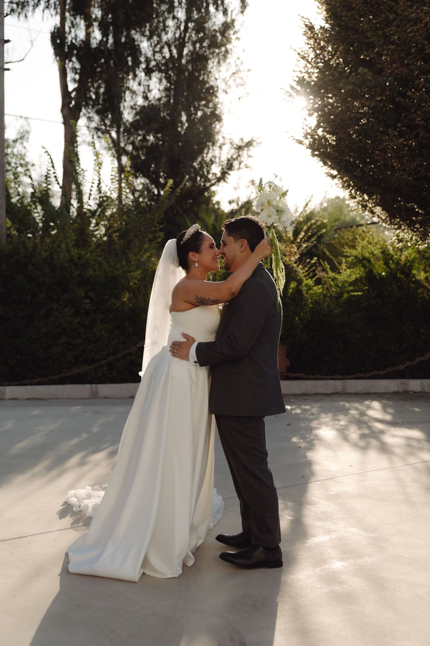 Bride and groom embracing romantically in a sunlit garden on their wedding day.