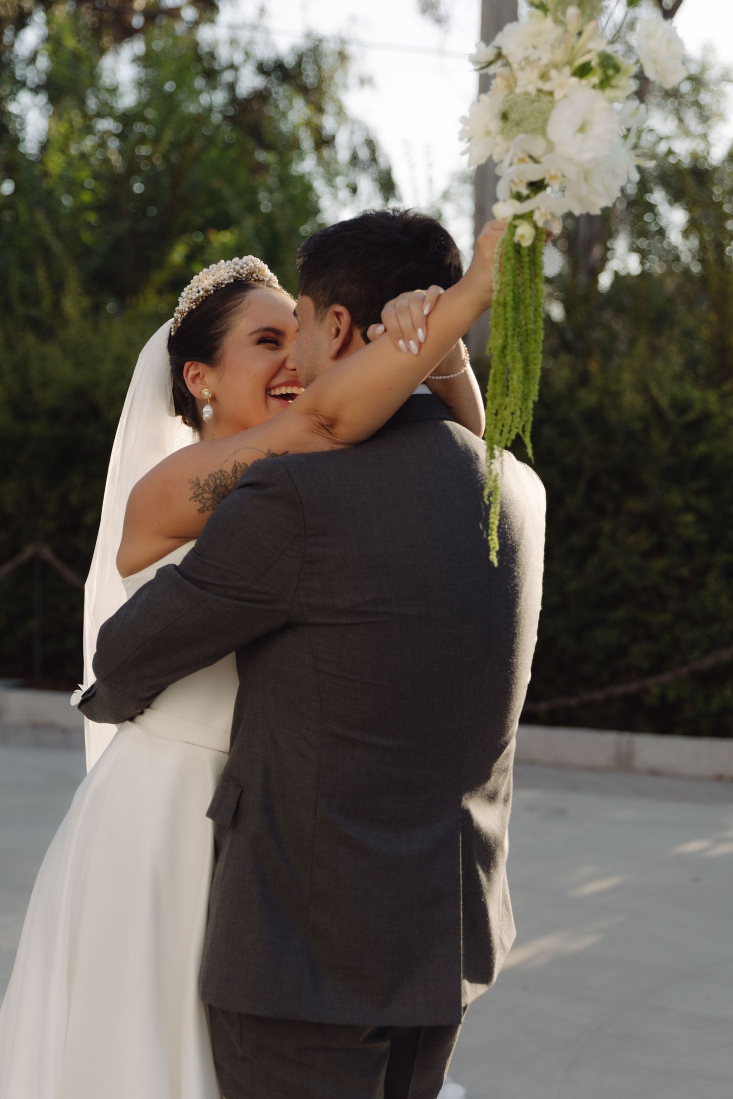 Joyful bride hugging her groom while holding a white bouquet outdoors.