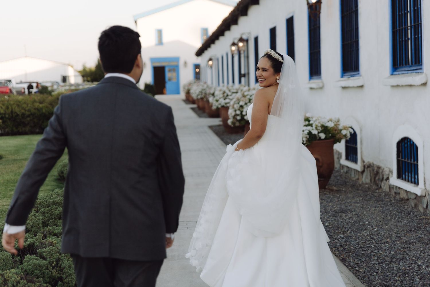 Bride and groom strolling together along a white building with blue shutters.