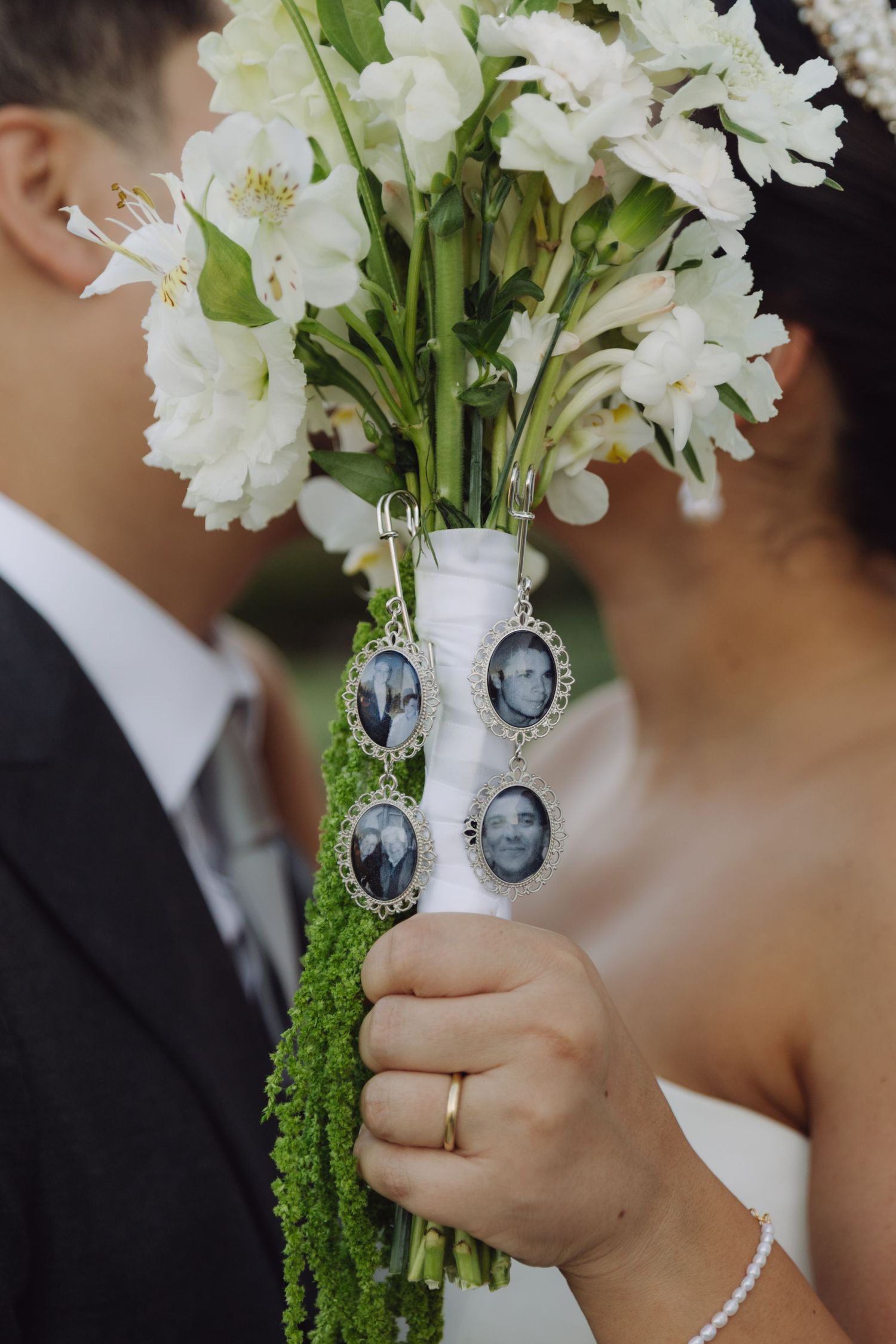 Close-up of bridal bouquet of white flowers adorned with black and white memorial photo charms.