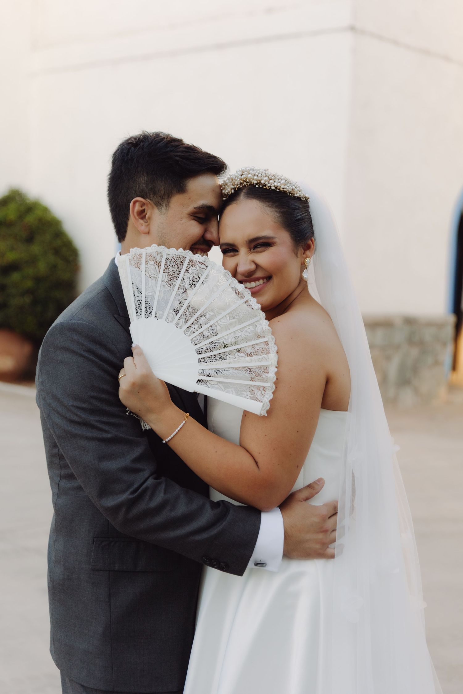 Bride and groom embrace holding a lace fan on their wedding day.