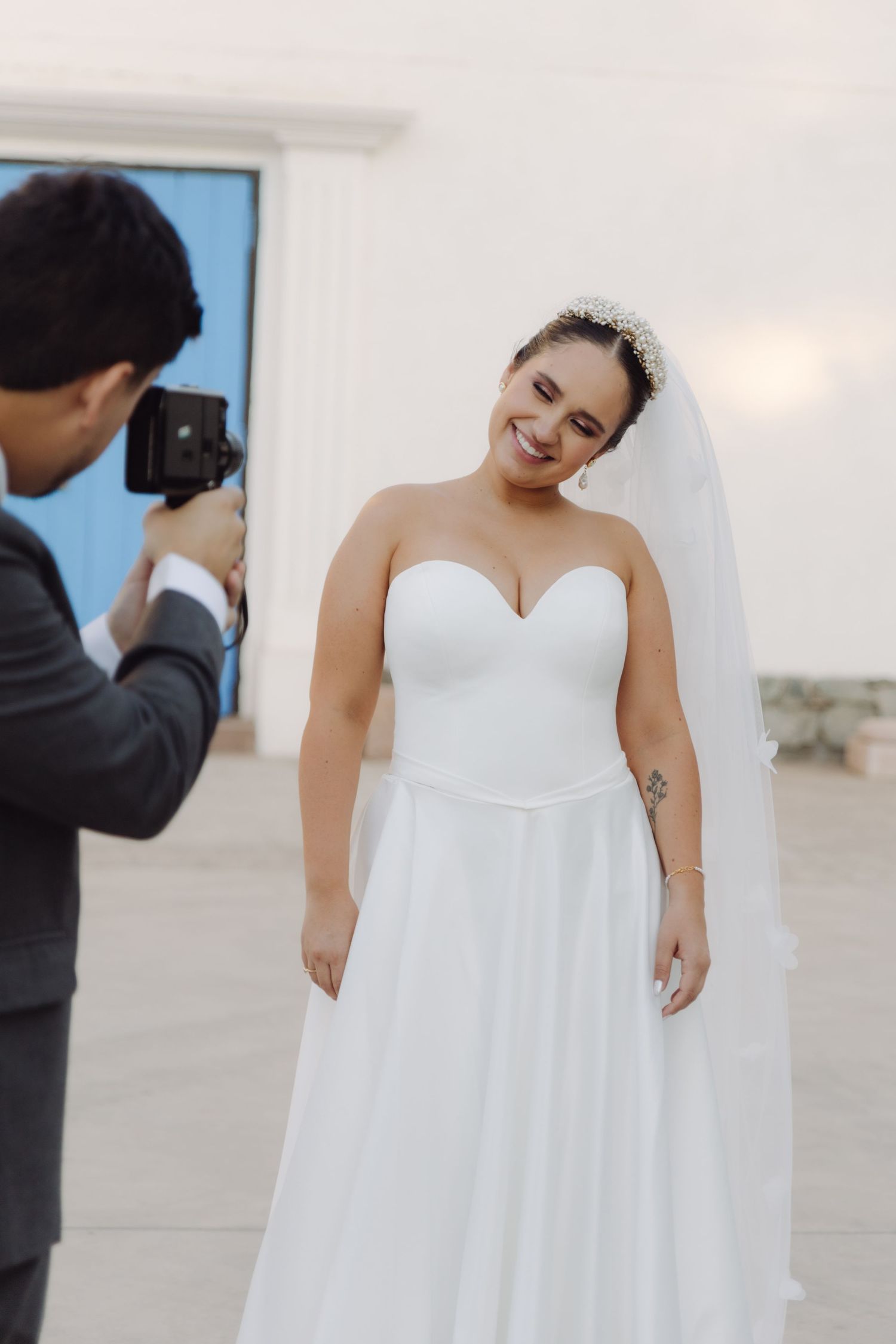 Photographer captures smiling bride in strapless white gown and veil.