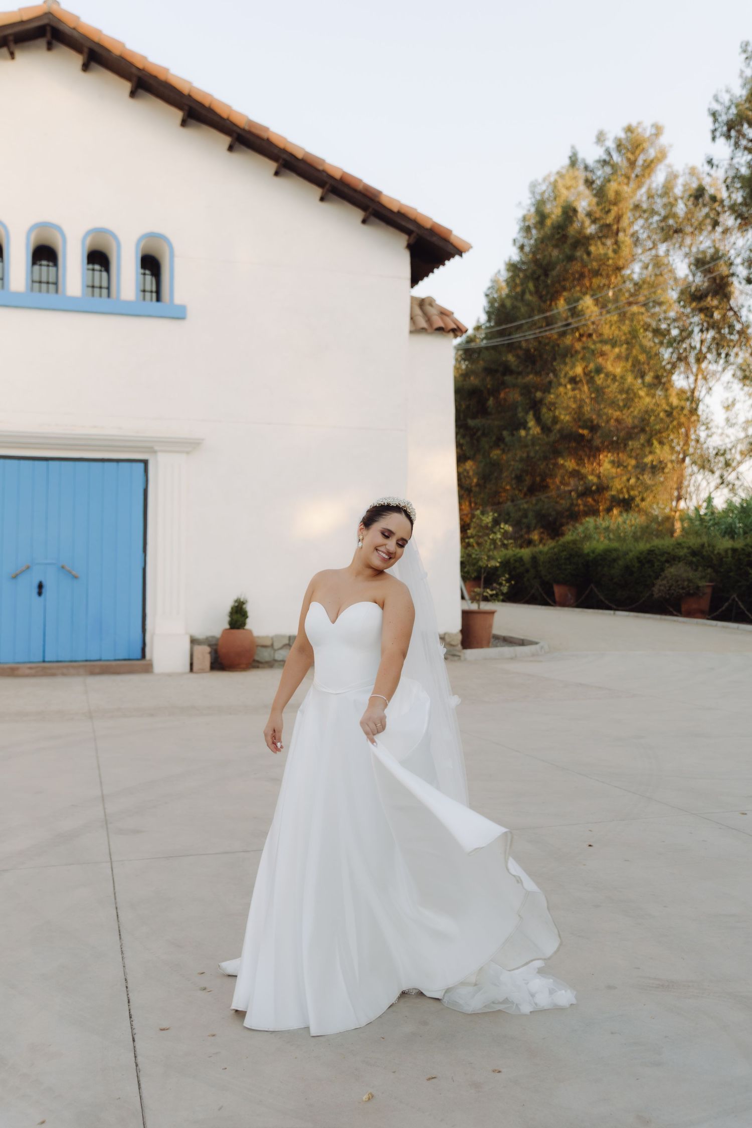 Bride in strapless white gown twirls outside a white Spanish-style building.