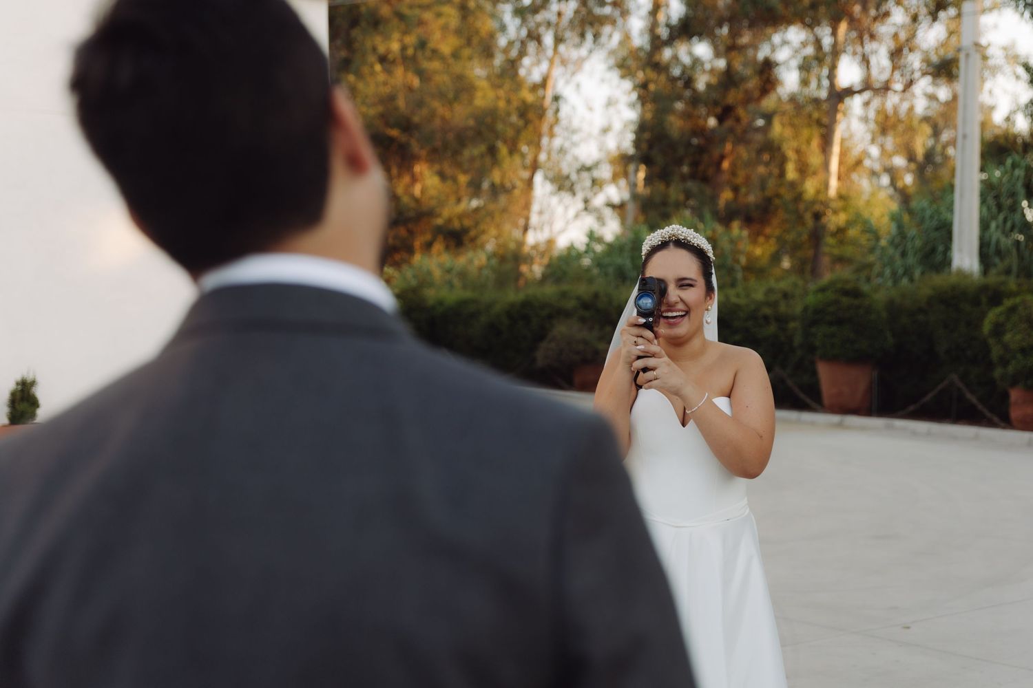 Bride in white gown photographs groom in gray suit at golden hour.