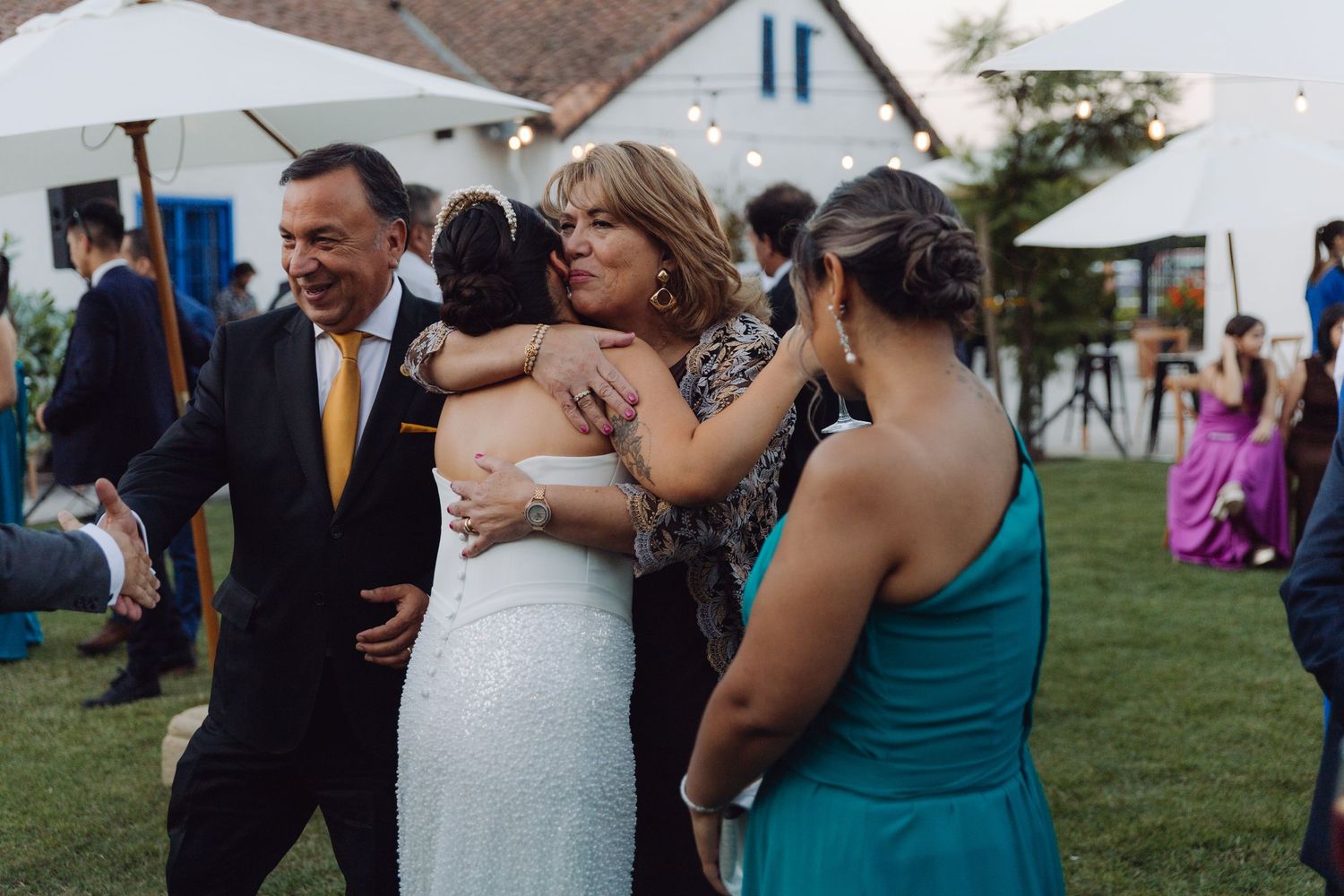 Bride receives warm hugs from family members at outdoor wedding reception.