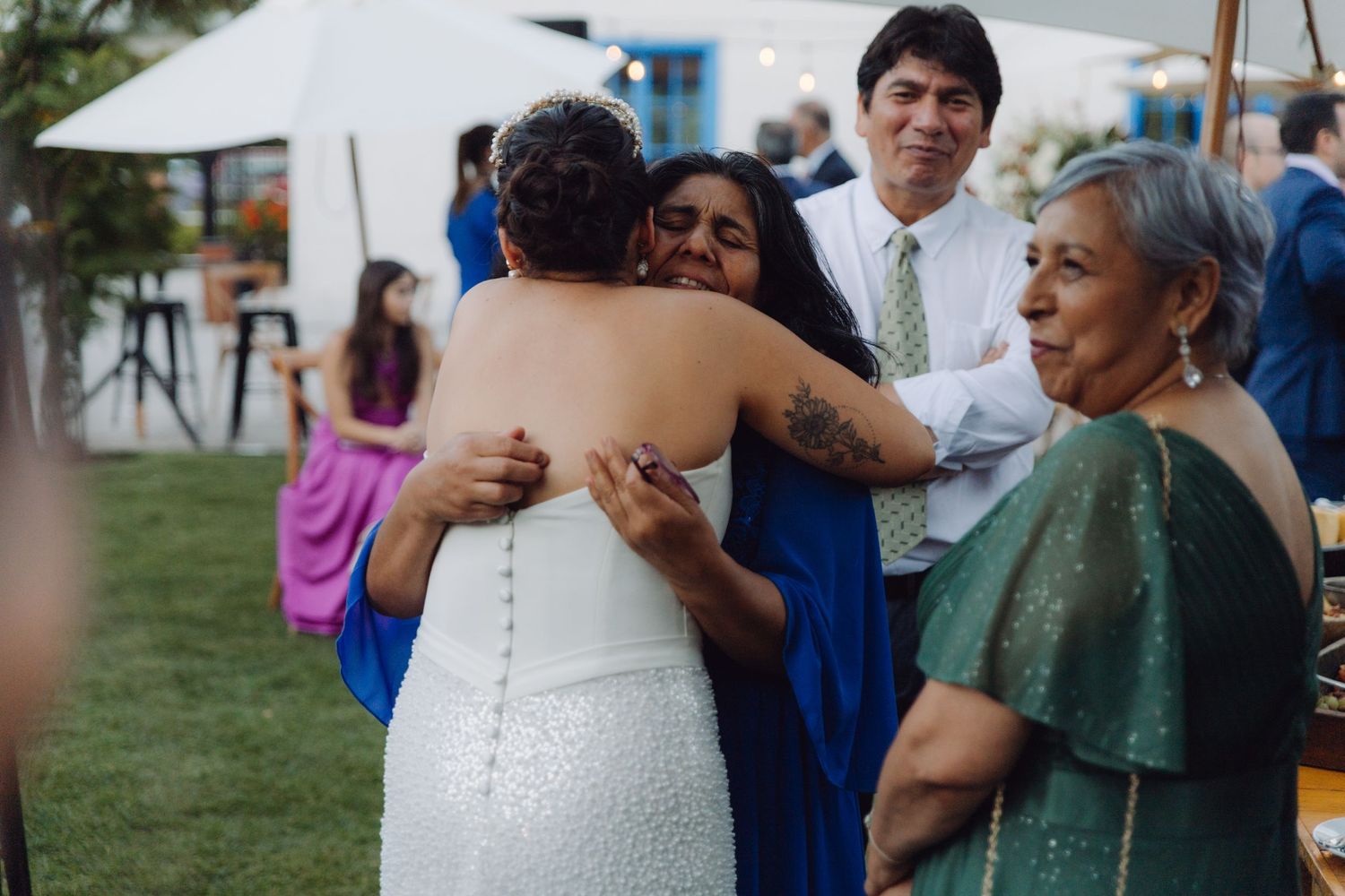 Wedding guest in blue dress embraces the bride warmly at an outdoor reception celebration.