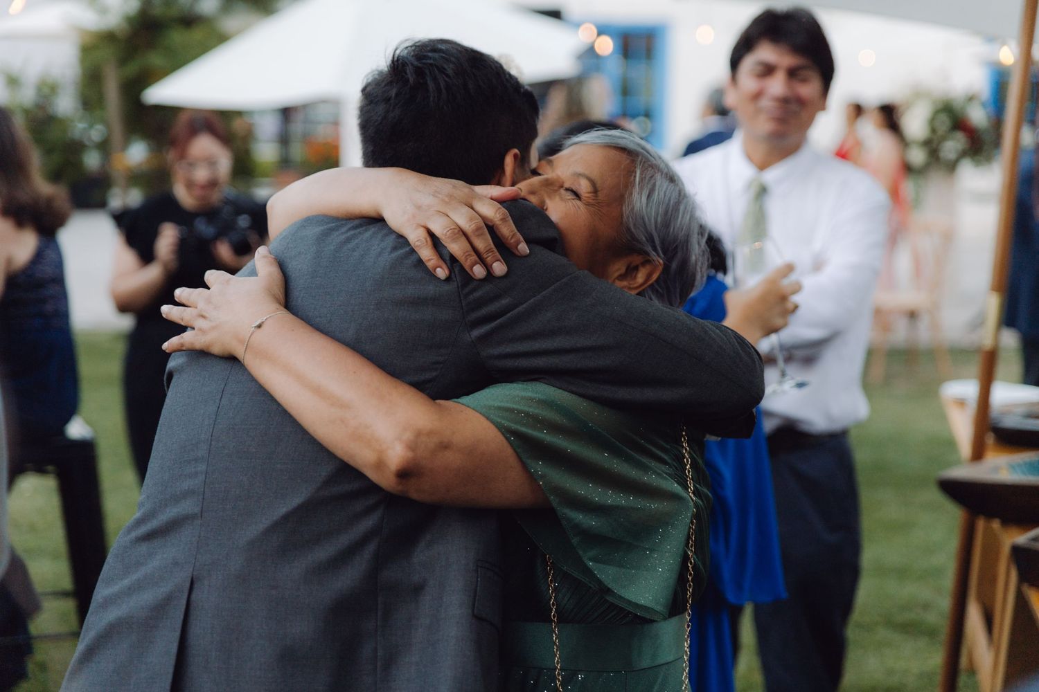 Two guests share a heartfelt hug at an elegant outdoor wedding reception under a tent.