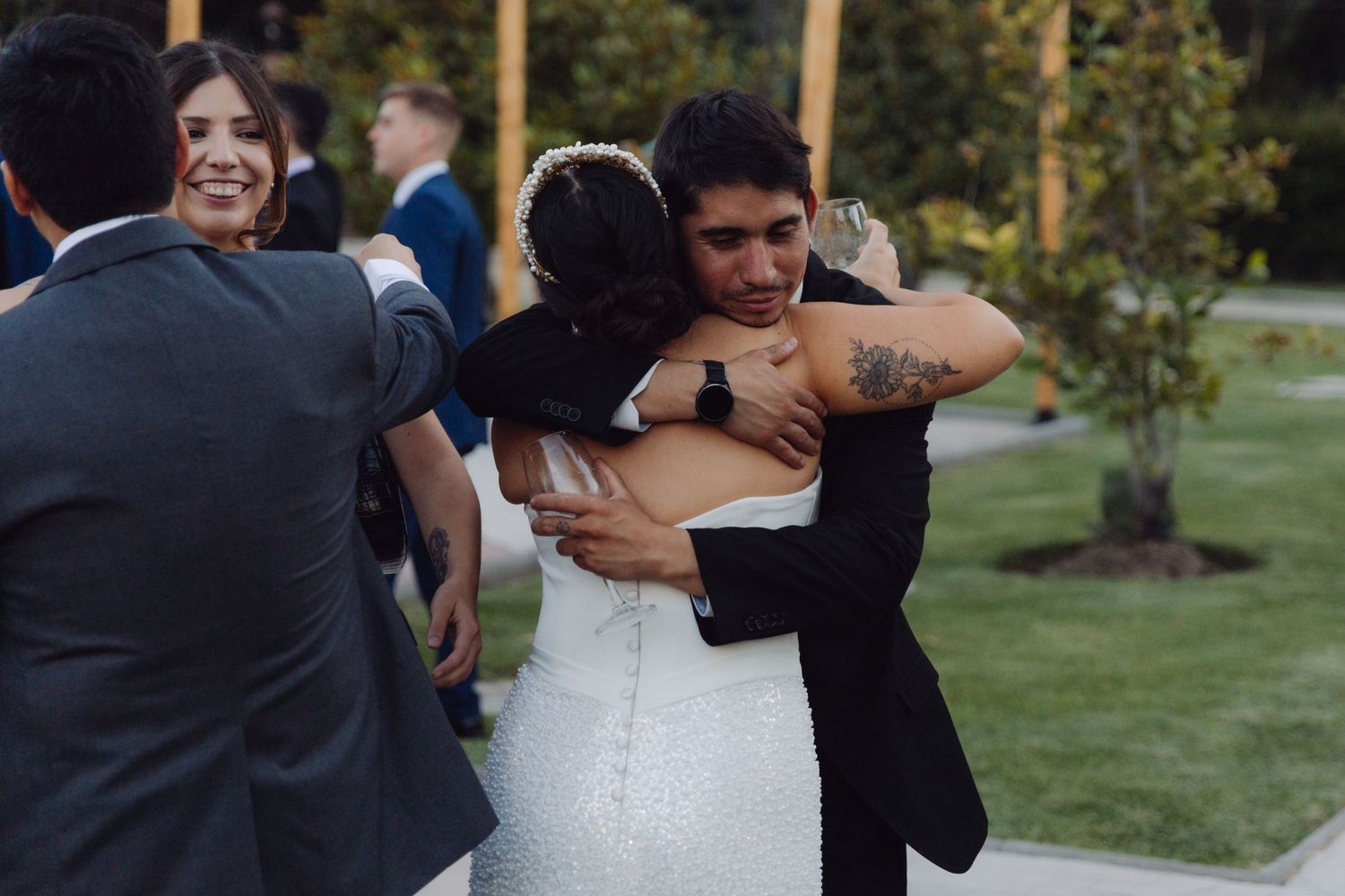 Bride and groom share a warm embrace with a guest at their outdoor wedding reception.