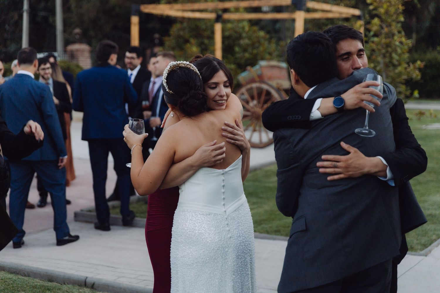 Bride in white gown hugs guests while others socialize at an elegant outdoor wedding reception.