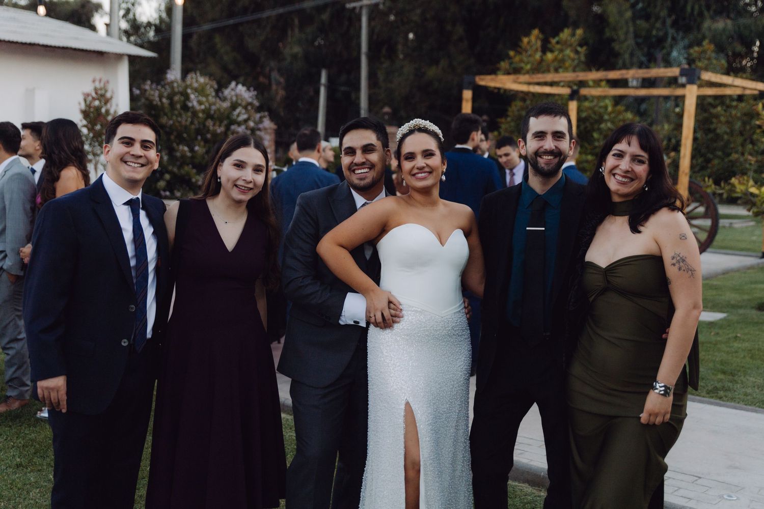 Bride and groom pose with four friends for a group photo at their outdoor wedding celebration.