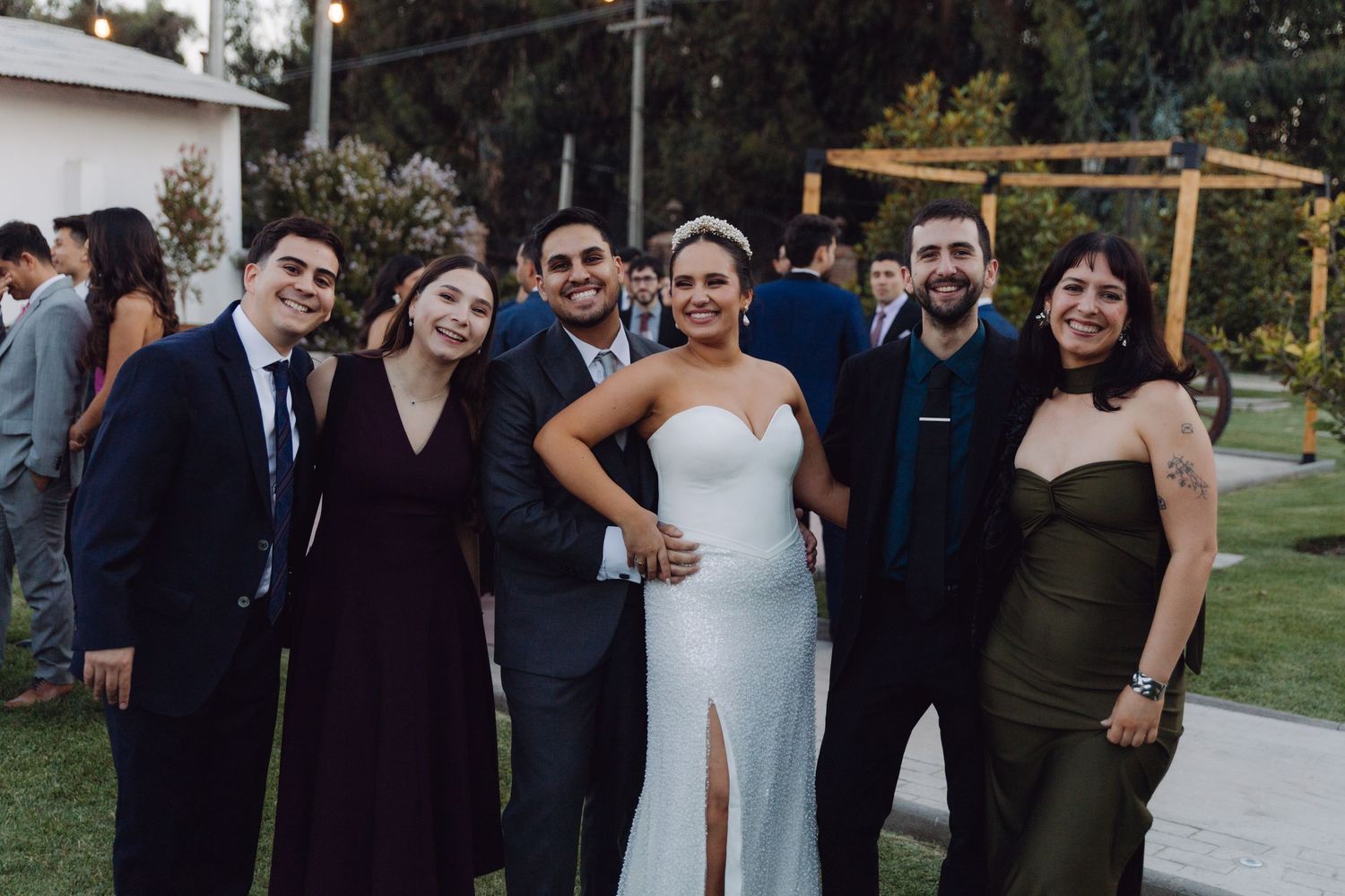 Bride and groom smile with four guests in formal attire at an outdoor wedding reception.