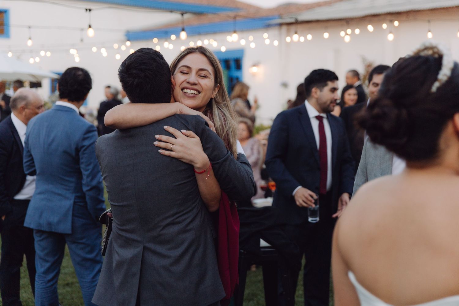 Smiling woman in burgundy dress hugs a guest at a festive outdoor wedding reception.