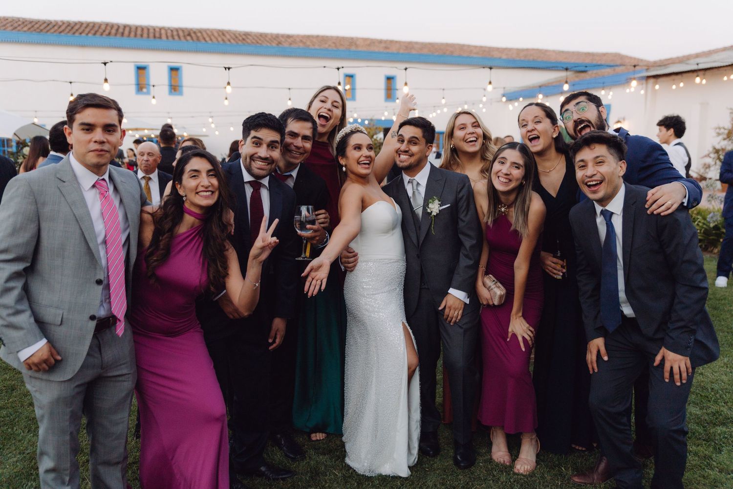 Bride and groom pose with a large group of smiling friends at an outdoor wedding reception.